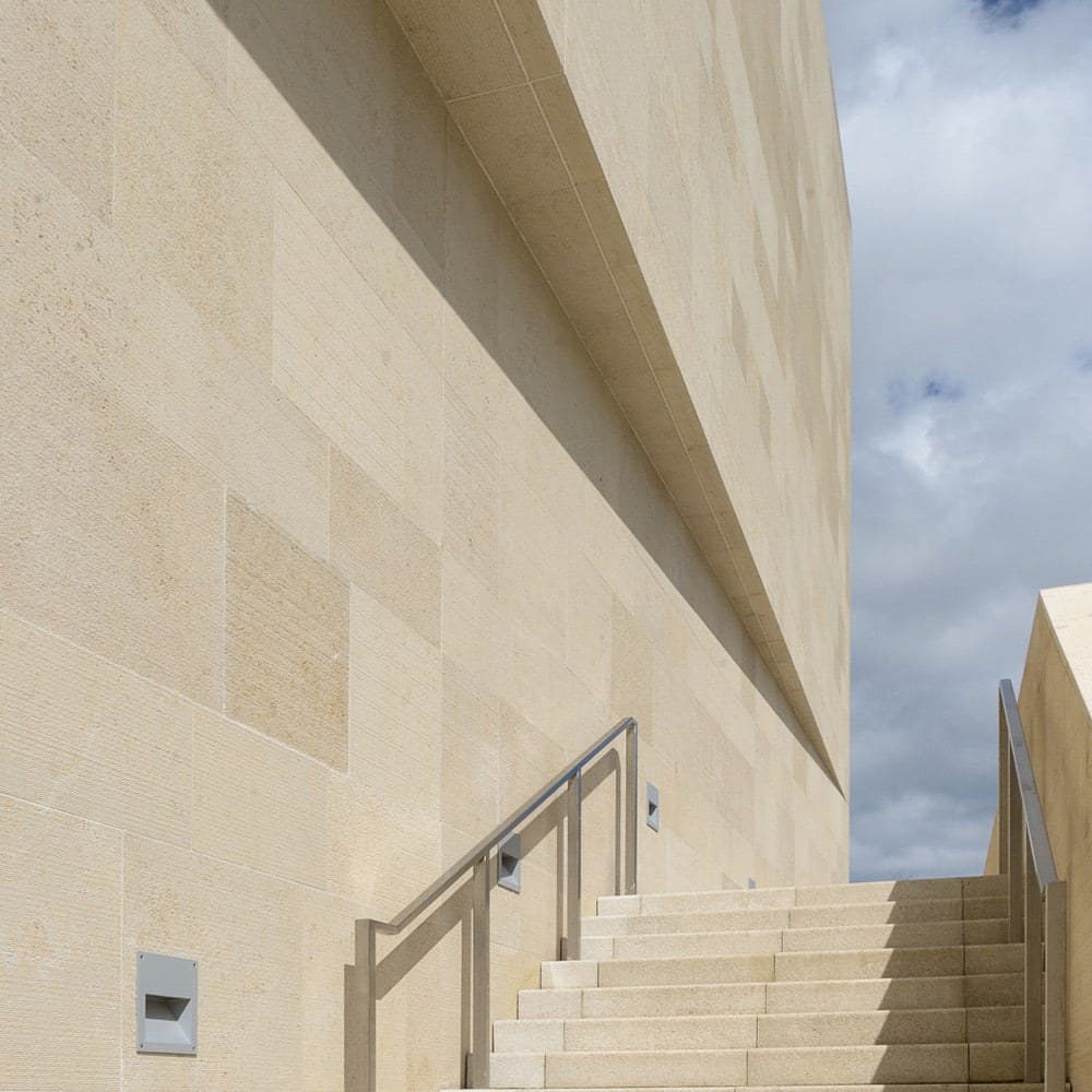 Fachada revestida en placas de Jura Beige sobre una escalinata de acceso