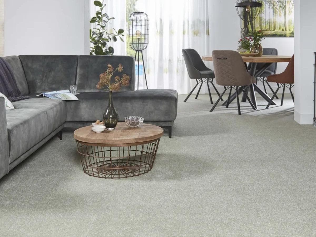 Living con alfombra de pared a pared en tono claro, sillón esquinero gris y comedor al fondo