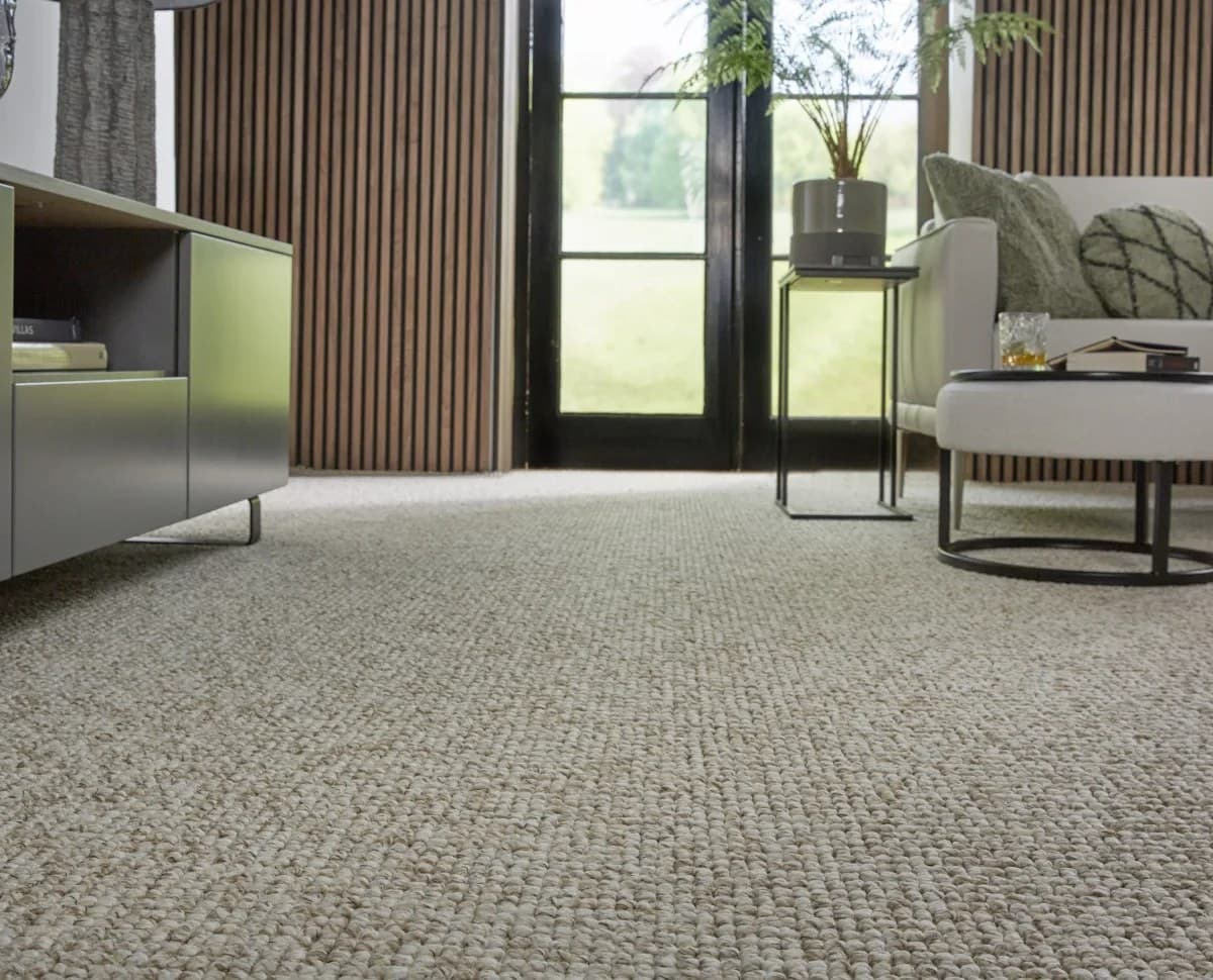 Living con alfombra bouclé de pared a pared, ventanal al jardín y sillón claro