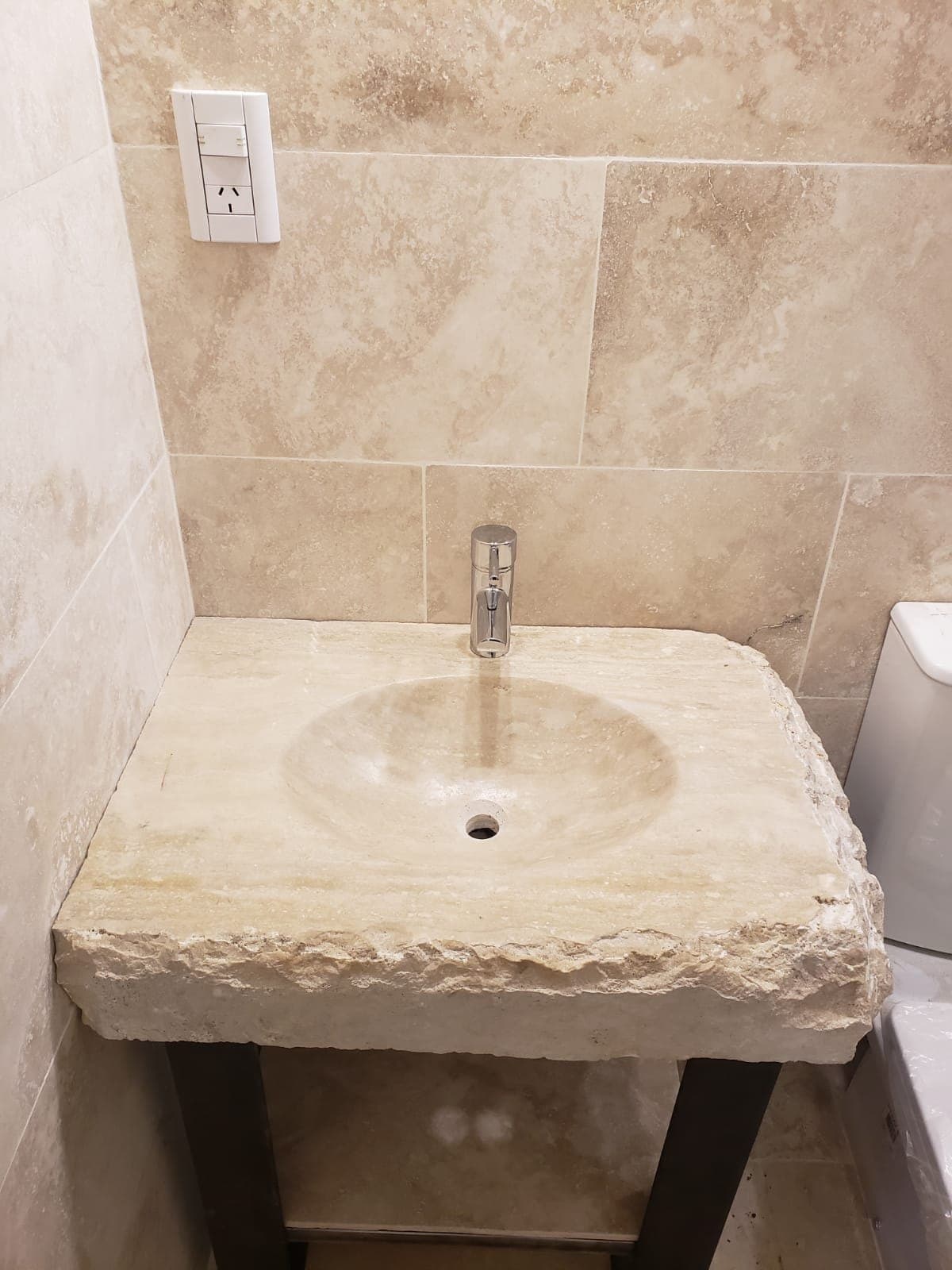 Bacha tallada en travertino sobre su pie, con la pared del baño en la misma piedra