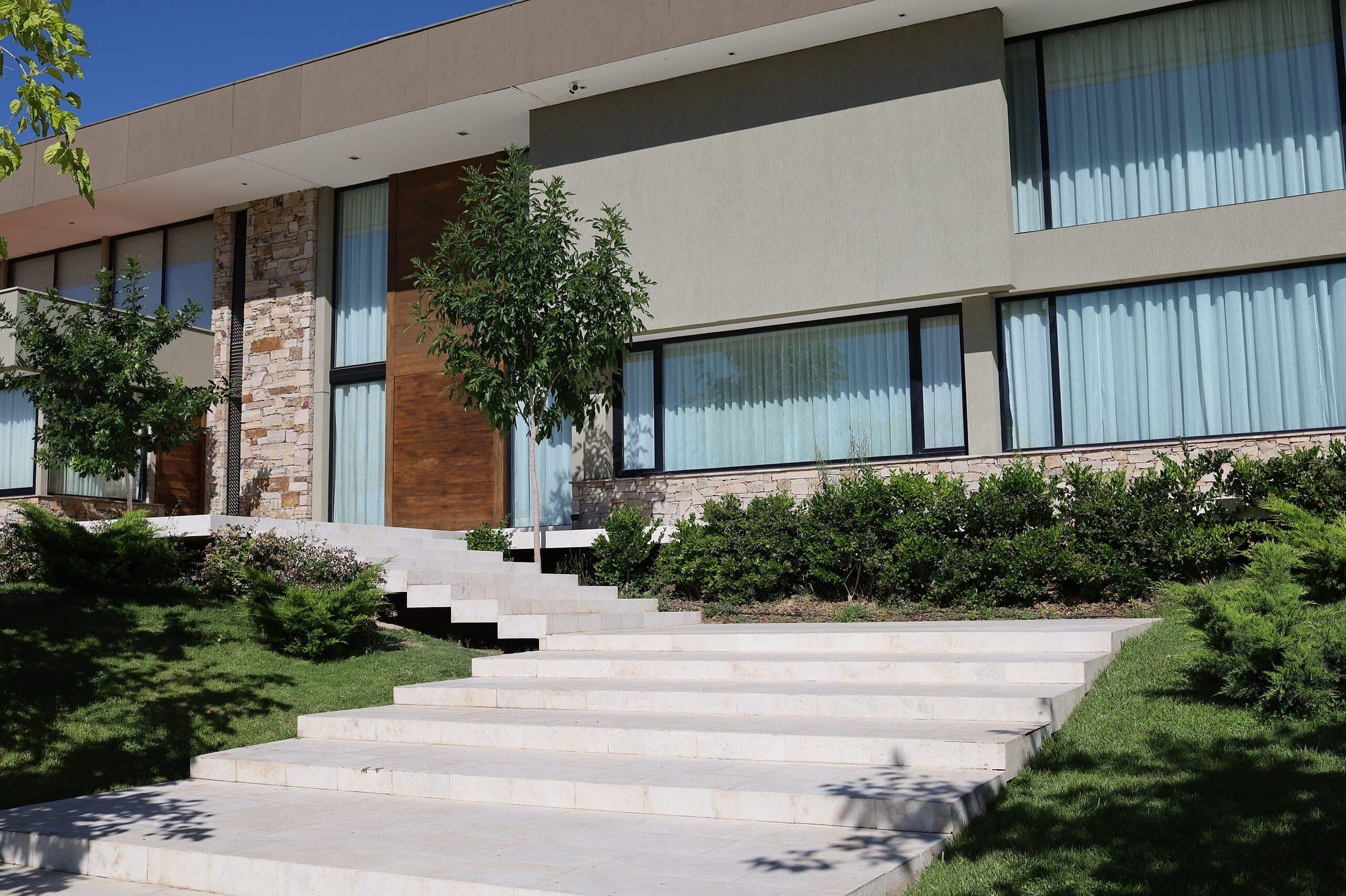 Escalera exterior de travertino que sube entre el jardín hasta la entrada de una casa