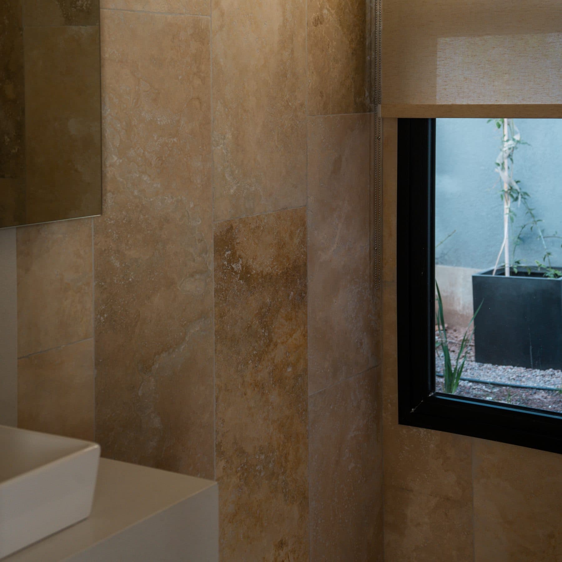 Pared de baño revestida en placas de travertino de tono dorado, junto a una ventana