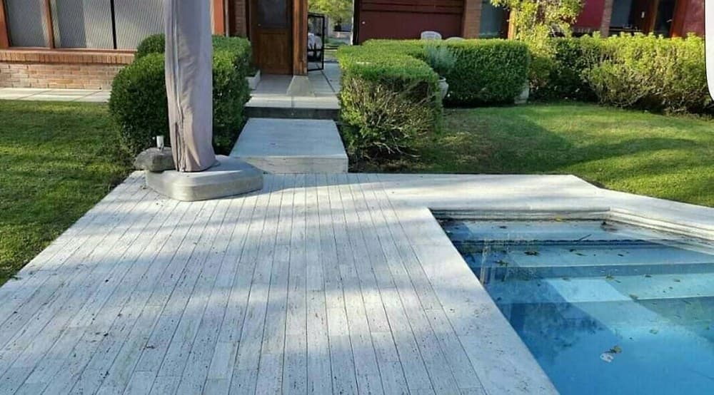 Solado exterior en travertino con terminación rústica junto a una pileta